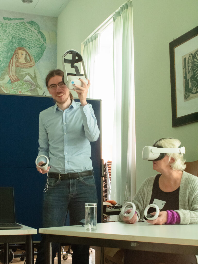 Einblick in den Workshop von fuels. Ein Frau hat eine VR-Brille auf und hält die Controller in der Hand. Eine weitere Person hat eine VR-Brille in der Hand.